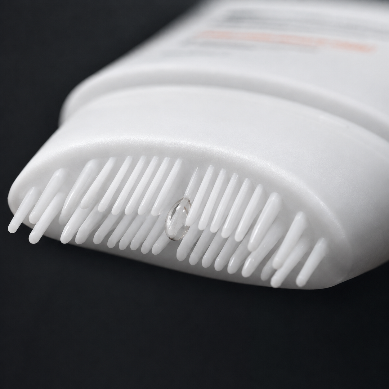 Close-up of the silicone scalp comb applicator teeth with a bead of serum